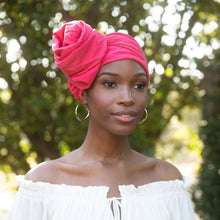Load image into Gallery viewer, A woman outdoors wearing a bright pink fabric Saqpphire Boho turban and an off-the-shoulder white blouse, with gold hoop earrings and bracelets. The background is a softly blurred green outdoor setting.