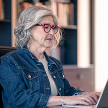 Load image into Gallery viewer, Side view of woman wearing a wig for hair loss. "Liz" by La Vida Wigs, talking on a phone in an office setting with books and a laptop.