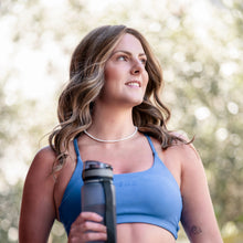 Load image into Gallery viewer, Woman wearing the "Marissa" wig. She is dtressed in blue athletic wear standing outdoors with greenery in the background