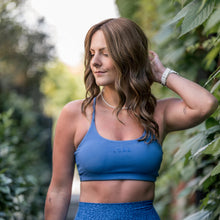 Load image into Gallery viewer, Woman wearing the "Marissa" wig. She is dtressed in blue athletic wear standing outdoors with greenery in the background